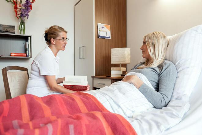 Ausbildung zur Hospizbegleitung Eine Ehrenamtliche sitzt am Bett einer Frau.