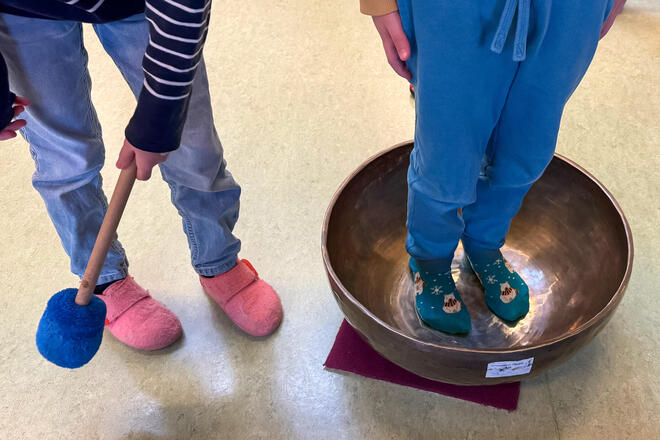 Musiculum MOBIL im Quickelbü Ein Kind steht in einer Klangschale, während ein anderes Kind dagegen schlägt.