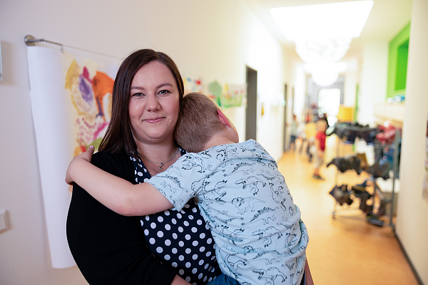 Eine Erzieherin in einer Johanniter-Kita trägt ein Kind auf dem Arm. Sie lächelt freundlich in die Kamera.