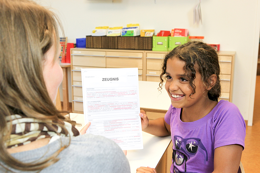 Lächelndes Mädchen zeigt einer Erwachsenen ihr Zeugnis.