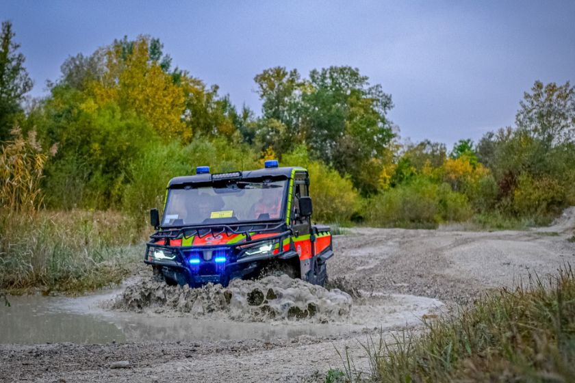 Ein Johanniter-Spezialfahrzeug fährt mit eingeschaltetem Blaulicht durch eine schlammige Pfütze auf einem Feldweg.