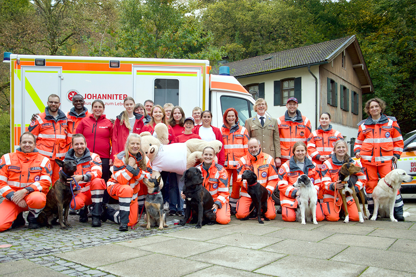 Gruppenfoto von Johannitern in Einsatzkleidung mit Rettungshunden vor Einsatzfahrzeug.