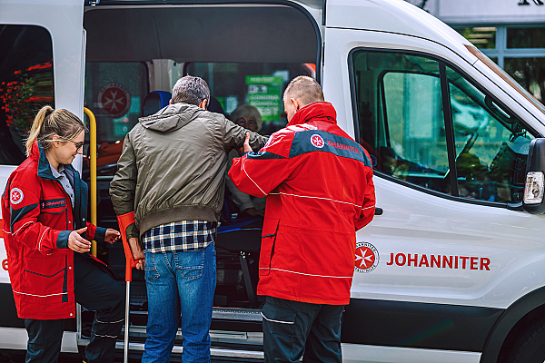 Johanniter Fahrdienst Mitarbeiter helfen einen älteren Mann in das Fahrdienst Auto