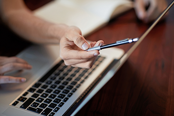 Junger Mann zeigt mit seiner Hand auf den Monitor eines Laptops.