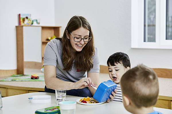Eine Frau sitzt mit einem Kind am Tisch und gibt Mittagessen auf.