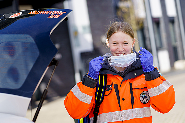 Rettungskraft in Uniform setzt ihre Maske auf.