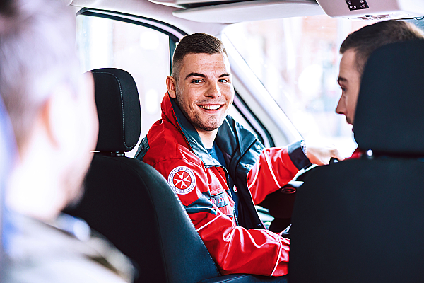 Junger Mann vom Fahrdienst spricht mit Klienten im Wagen.
