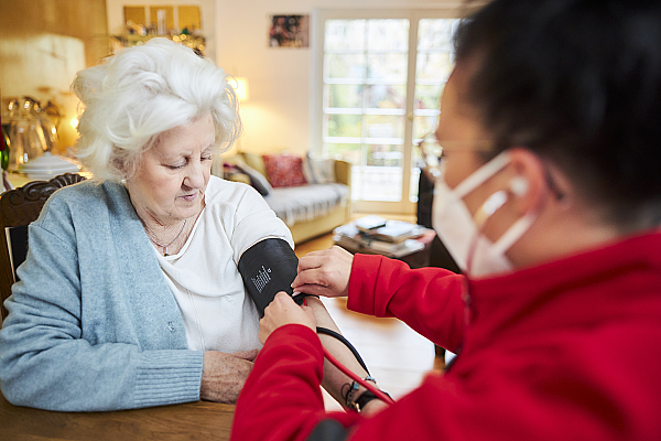 Eine junge Mitarbeiterin der ambulanten Pflege misst den Blutdruck einer Patientin