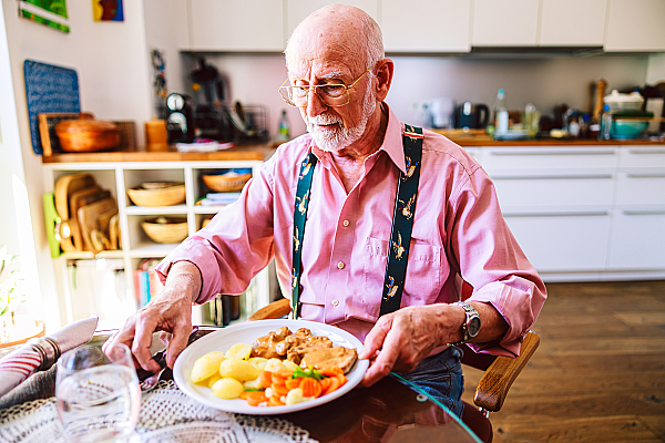 älterer Mann mit Essen vom Menüservice 