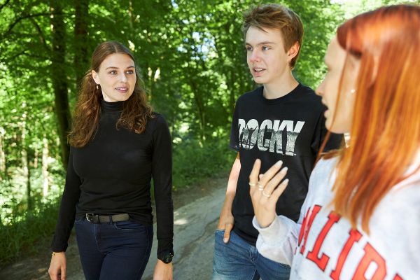 Junge Sozialarbeiterin geht mit zwei gerade aus Wohngruppen ausgezogenen jungen Leuten. Das junge Mädchen erzählt ihr etwas.