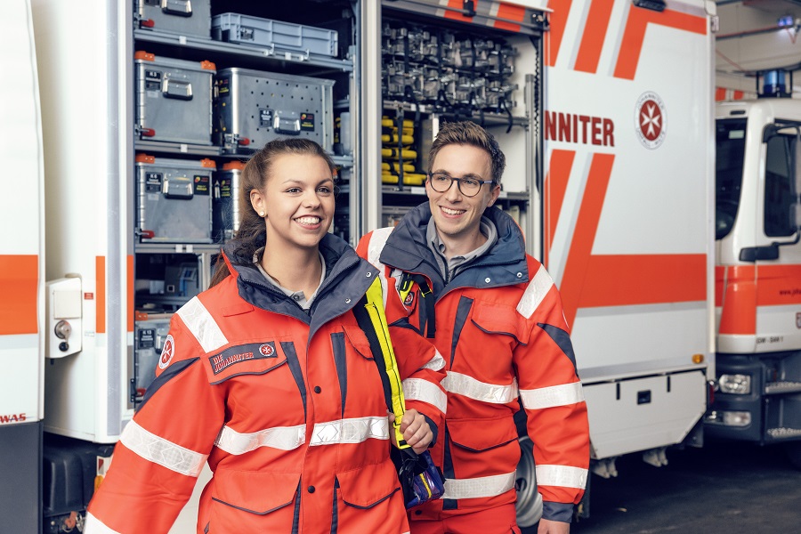 Zwei Ehrenamtliche der Johanniter vor einem Einsatzwagen