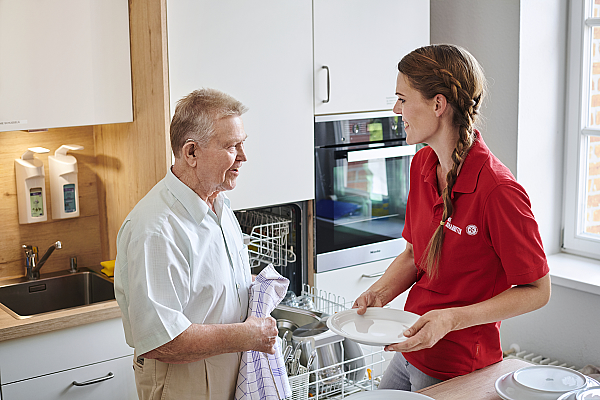 Eine Pflegekraft hilft einem Mann beim Abtrocknen von Geschirr
