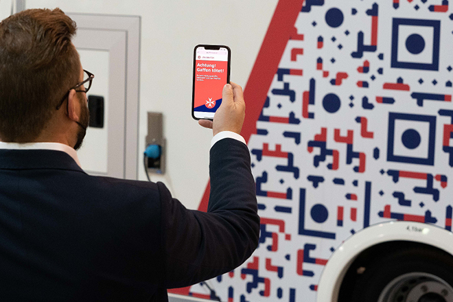 Ein Mann hält sein Handy hoch, um einen QR-Code auf dem Rettungswagen einzuscannen