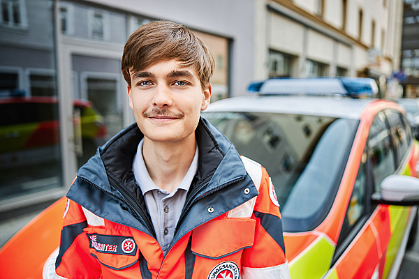 Ein junger Mann in Johanniter-Bekleidung vor einem Einsatzwagen