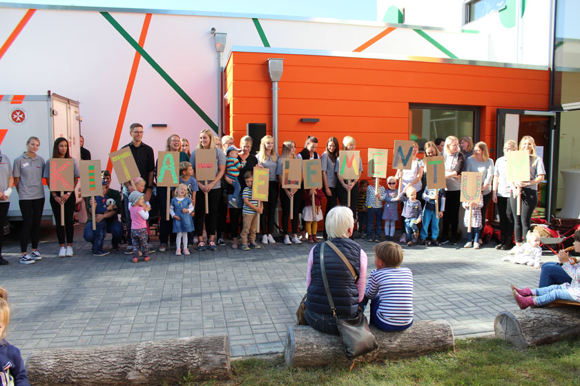 Kita-Kinder halten bei der Eröffnungsfeier selbstgebastelte Schilder mit Buchstaben hoch, auf denen der neue Kita-Name "Elementum" zu lesen ist.