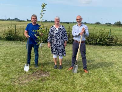 Amtsvorsteher Harm Schloe, Kita-Leitung Tanja Burkhard und der leitende Verwaltungsbeamte Christopher Stein mit dem zu setzenden Apfelbaum