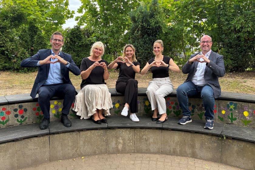 Fünf Personen (u.a. der Bürgermeister von Erkrath und die Landrätin des Kreises Mettmann) sitzen im Garten auf einer Bank und formen mit den Händen ein Herz.
