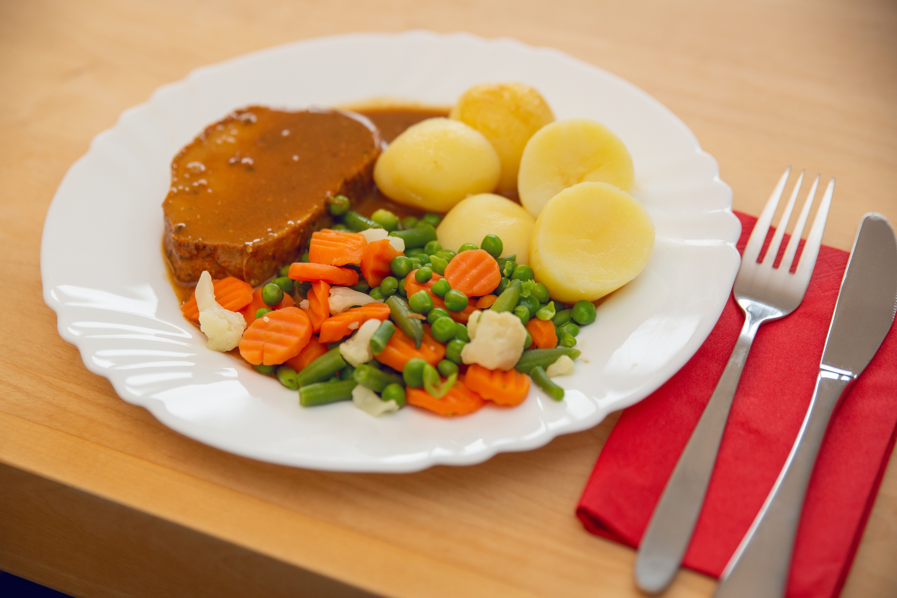 Ein Teller mit Kartoffeln, Braten und Kaisergemüse auf einem Tisch