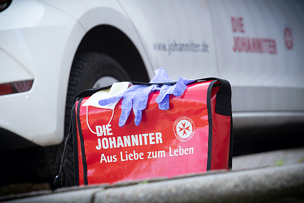 Mund-Nasen-Schutz und Einmalhandschuhe liegen auf einer roten Johanniter-Tasche. 