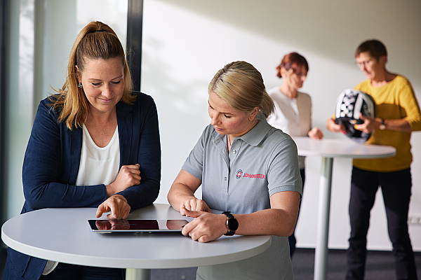 Eine Erste-Hilfe-Ausbilderin der Johanniter zeigt einer Kurs-Teilnehmerin etwas auf einem Tablet.