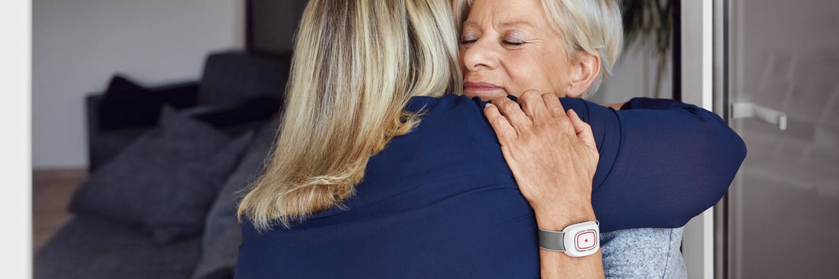 Eine Hausnotrufkundin mit Handsender umarmt eine Frau.