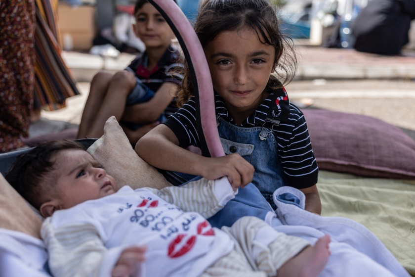 Ein Mädchen hält die Hand eines Babys, das neben ihr auf Decken liegt.