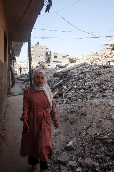 Eine Frau mit Kopftuch steht vor den Trümmern eines eingestürzten Gebäudes.