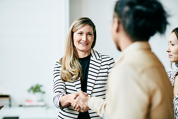 Eine Geschäftsfrau schüttelt lächelnd die Hände einer Klientin vor einem Meeting.