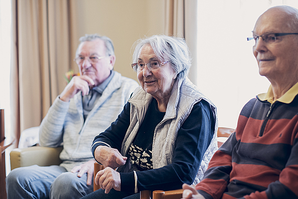 Drei Bewohnende lauschen einer Person im Gruppenangebot