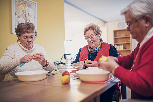 Drei Bewohnerinnen sitzen an einem Tisch und schälen Äpfel