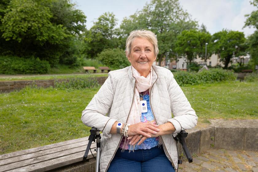 Frau im Rollstuhl mit Hausnotrufgerät im Park