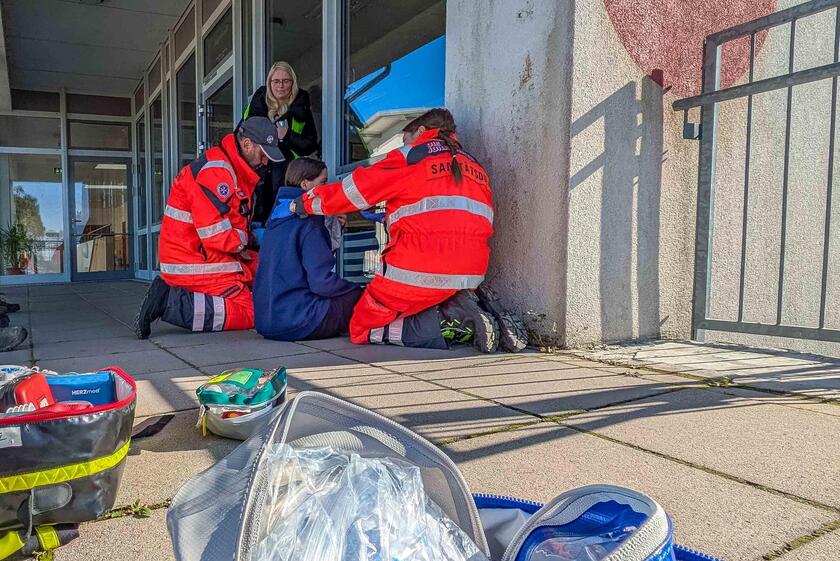 Zwei Sanitätsdienstleistende kümmern sich um eine Person, die im Schatten sitzt.