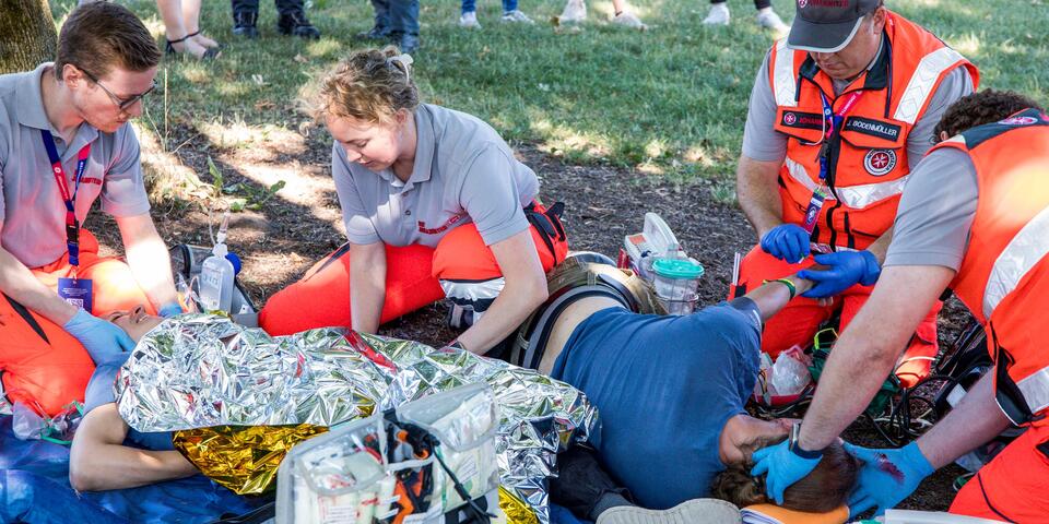 Rettungshelfer*innen behandeln im Freien mehrere gestellte Patient*innen mithilfe medizinischer Ausrüstung.