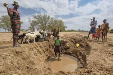 Menschen stehen um ein ausgetrocknetes Wasserloch herum.