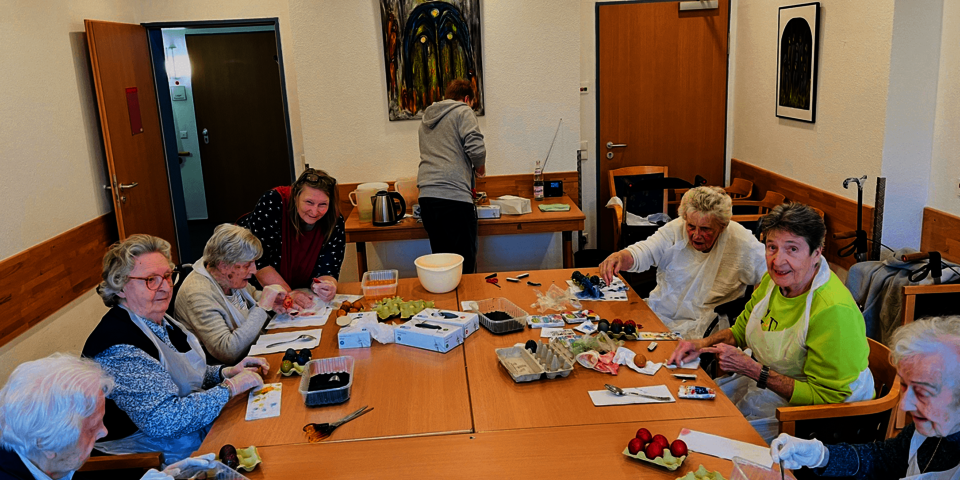 Gruppe von Menschen sitzt mit Malutensilien um einen Tisch