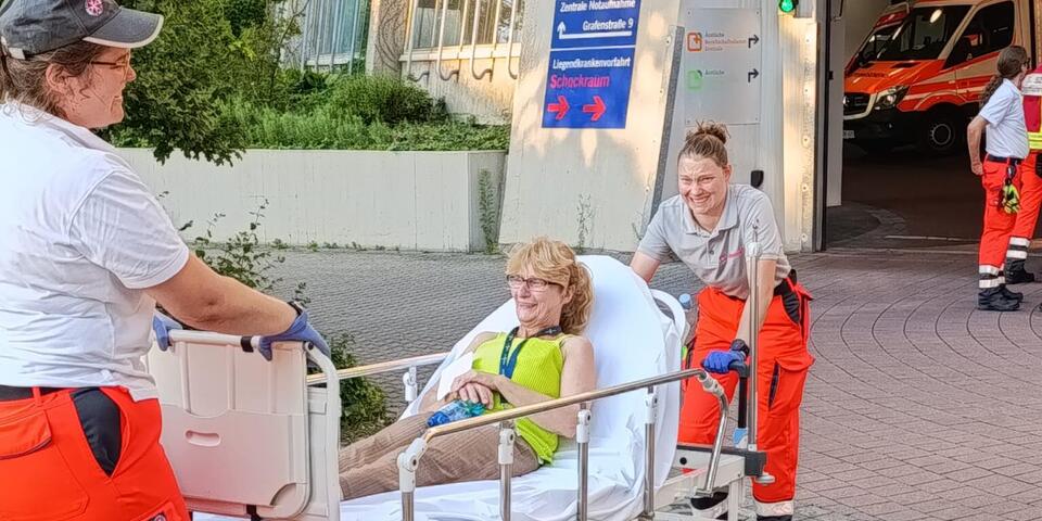 Transport einer Mime im Patientenbett durch zwei Einsatzkräfte zu den Einsatzfahrzeugen