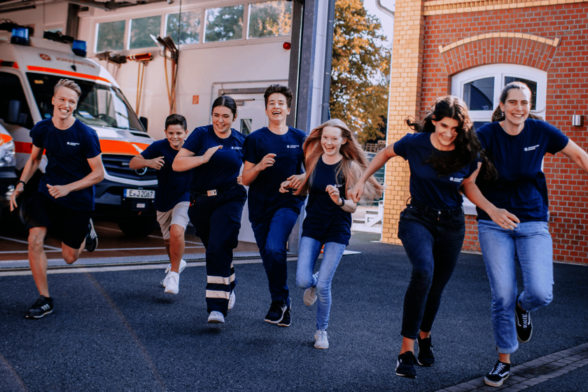 Eine Gruppe junger Menschen in dunkelblauen T-Shirts laufen gutgelaunt über einen Hof
