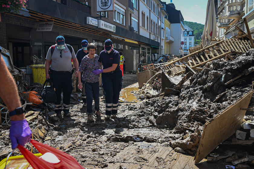 Einsatzkräfte im Ahrtal helfen einer Betroffenen durch die verwüstetete Straße