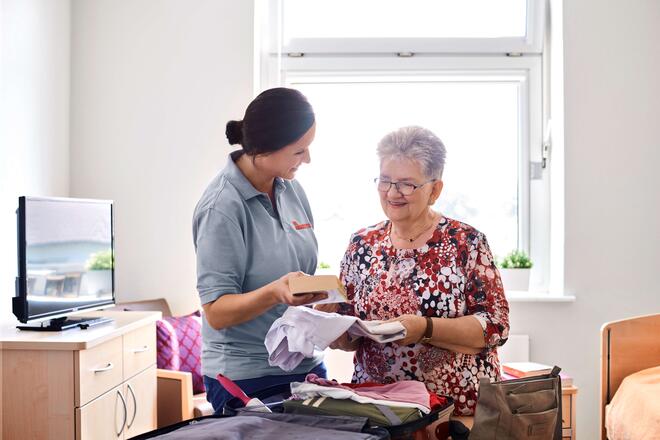 eine Pflegekraft hilft einer Seniorin beim Auspacken des Koffers