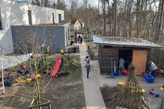 Das Bild zeigt den Garten der Kita. Hier arbeiten Kinder und Erwachsene und bringen den Garten auf Vordermann.