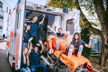 Jugendliche der Johanniter-Jugend am Ende eines Rettungswagen schaffen eine Playmobilfigur auf einer Trage in den Rettungswagen.