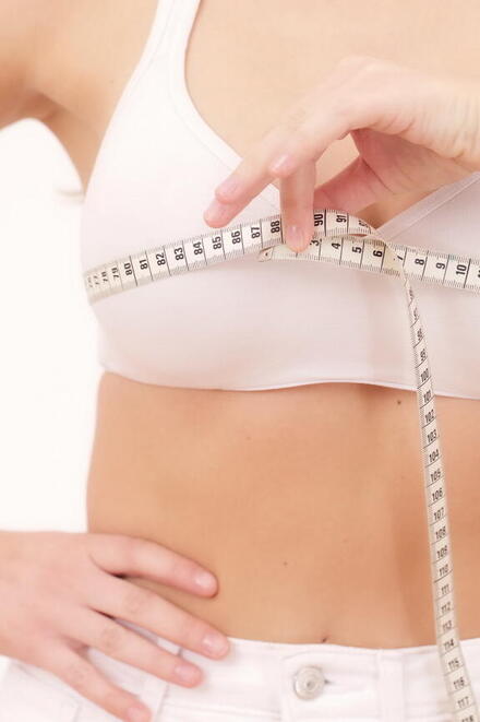 Frau die mit einem Maßband ihren Brustumfang misst 