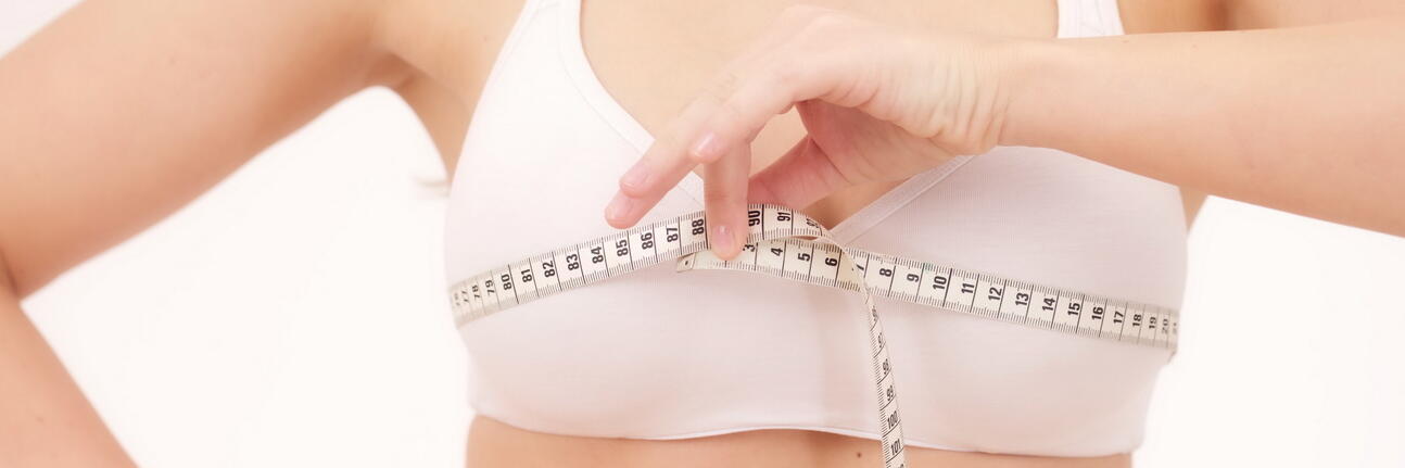 Frau die mit einem Maßband ihren Brustumfang misst 
