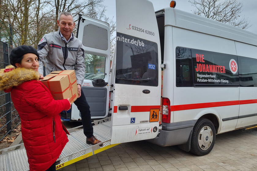 Frau Nino Benne übergibt Ralf Boost auf einer Rampe zu einem Transporter des Fahrdienst ein Paket mit der Aufschrift "Weihnachtstrucker".