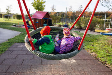 Zwei Kinder schaukeln gemeinsam in einer Korbschaukel auf dem Außengelände der Kita