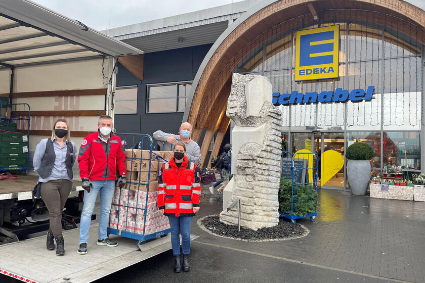 4 Personen vor einem LKW laden Materialien ein. Im Hintergrund ein Supermarkt