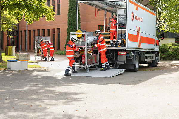 mehrere Ehrenamtliche in Einsatzkleidung verladen technisches Gerät in einen LKW