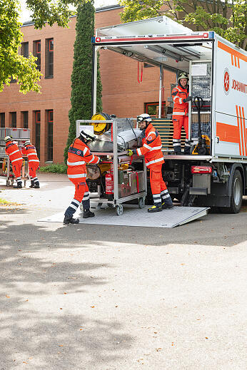 Johanniter-Rettungskräfte in Einsatzkleidung entnehmen Ausrüstung aus einem LKW