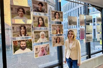 Abier Jamos, Leiterin der Kunstprojektes der Landesunterkunft, vor Portraits der Künstlerinnen und Künstlern im Pop-Up Pavillon Kiel.
