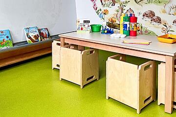 Niedrige Kindertische mit Holzstühlen und Spielmaterial in einem farbenfrohen Raum.